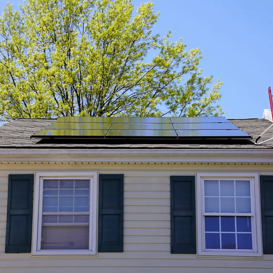 close up of home with solar panels on roof green shutters two windows