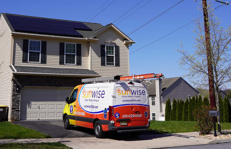 Sunwise service van parked outside a two-story home with a solar panel system installed on the roof.