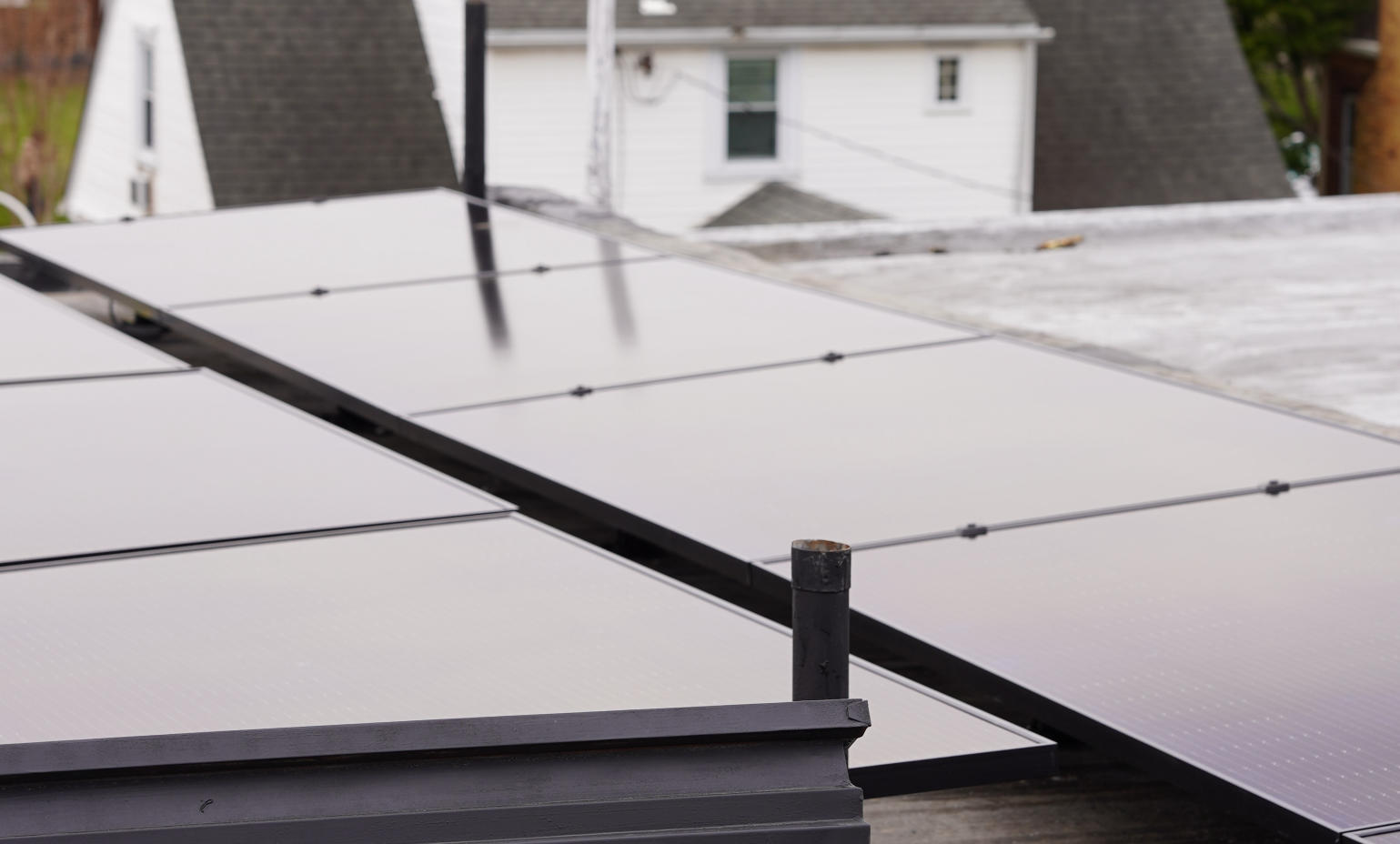 Close-up view of black solar panels installed on a flat residential roof with a white house in the background.